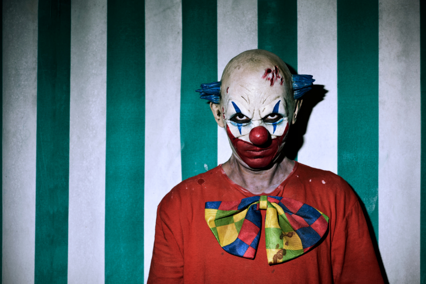 scary clown staring at you in front of green and white striped wall