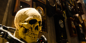 skeleton with neck chained to a shackle in front of a wall of old clocks