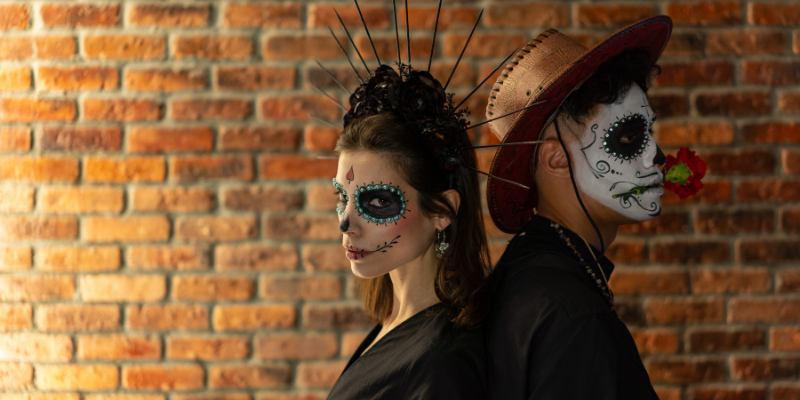 One man and woman standing back-to-back in decorative skull makeup.