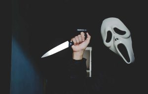 person in scream mask holding up a butcher's knife menacingly