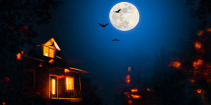 Haunted house in the night with a full moon in the sky and bats. Yellow candles illuminate the house.