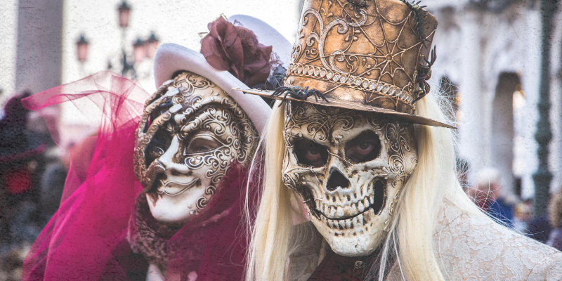 Two people wearing skull masks and elaborate costumes