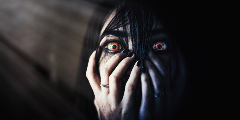 Woman with piercing orange eyes with her hands covering her face except her eyes.