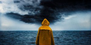 Person in a yellow rain slicker standing in front of a body of water with dark skies in the rain