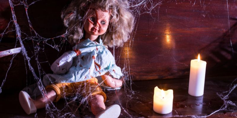 ragged doll covered in blood sitting on an abandoned floor surrounded by candles and cobwebs
