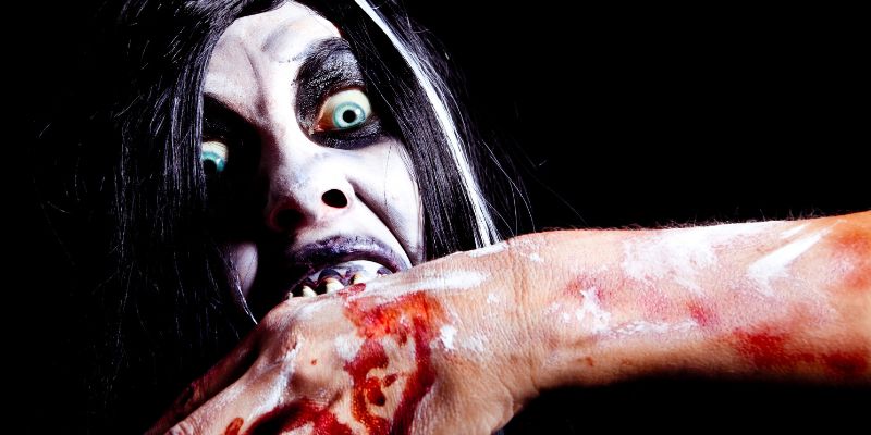 scary vampiric woman biting a bloodied arm