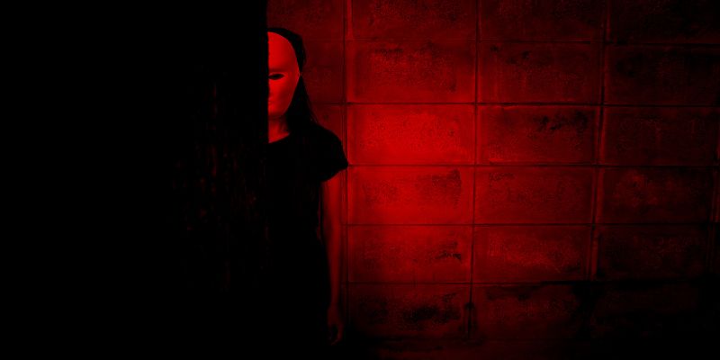 Woman wearing Jason Masks standing in red shadow. 
