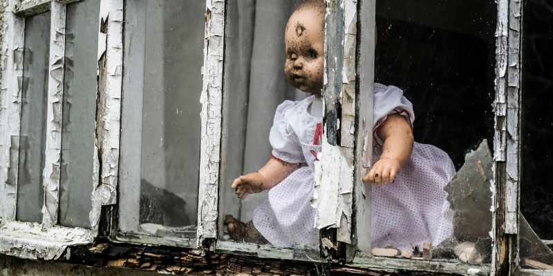 creepy baby doll sitting on rotting porch