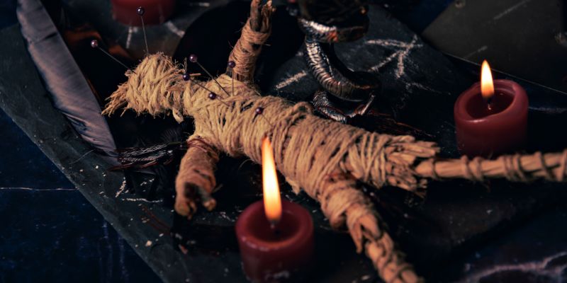 creepy voodoo doll surrounded by small lit candles