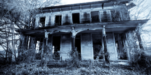 Black and white photo of a deteriorating house in the woods.