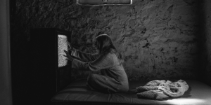 black and white image with young woman starring at laying hands on TV screen projecting static