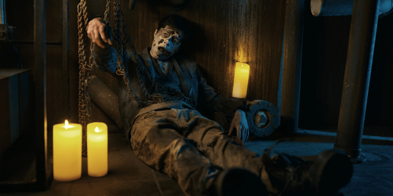 chained zombie surrounded by candles sitting in basement of abandoned house