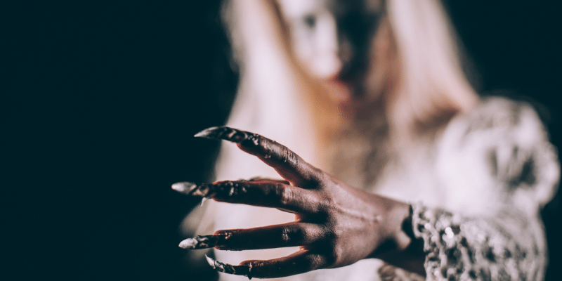 woman dressed as a witch standing in the night, with scary claw-nails