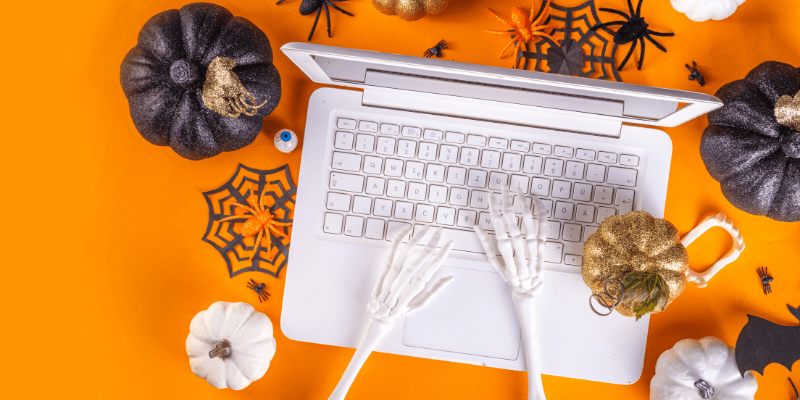 A bird's eye view photo of a laptop on an orange background and Halloween decor.