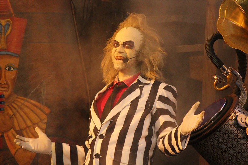 A man dressed as the character "Beetlejuice" while on stage. He is wearing a black and white striped suit, with a face painted with white makeup.