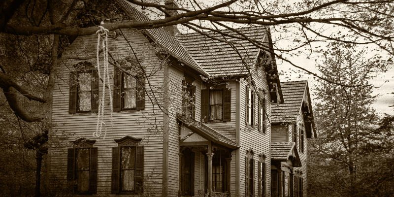 A rope noose hanging from a tree in front of the side view of a house.
