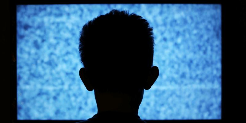 Silhouette of the back of a child's head while looking forward at TV static.