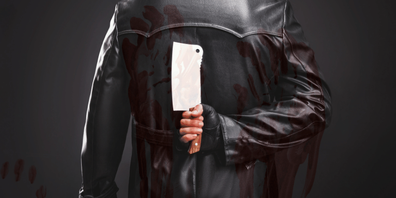 Man holding a butcher knife behind his back with red bloody handprints behind.