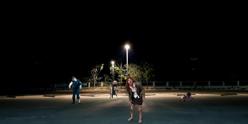 Four zombies approaching you in a dimly lit parking lot at night